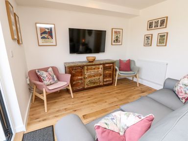 A living room with two armchairs a wooden cabinet under a wall-mounted TV and framed pictures on the wall at Chianti in Seaview