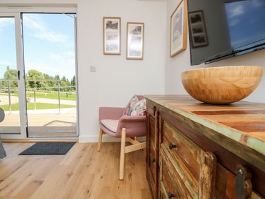A room with a wooden cabinet with a bowl on it a wall-mounted TV a pink chair and sliding glass doors showing an outdoor area at Chianti in Seaview