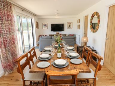 A dining table set with plates glasses and a wine bottle in a room with wooden chairs sofas and a wall-mounted TV at Chianti in Seaview