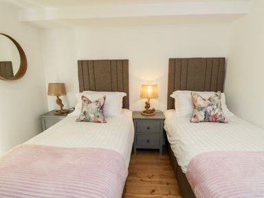 A bedroom with two single beds each with a brown headboard and floral pillow two bedside tables with lamps and a round wall mirror at Chianti in Seaview