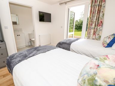A bedroom with two single beds a wall-mounted TV and an open door leading to a bathroom and a garden at Chianti in Seaview