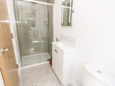 A bathroom with a shower enclosure, a sink with cabinet, a toilet, and a wooden door at Chianti in Seaview