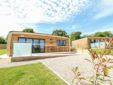 Two wooden lodges with glass doors and a ramp outside on a gravel and grass area at Chianti in Seaview