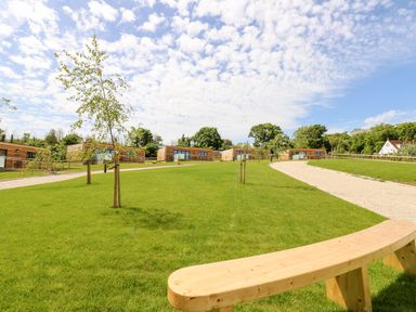 A grassy area with young trees and a wooden bench with wooden cabins in the background at Chianti in Seaview