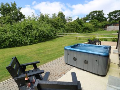 An outdoor area with a hot tub black chairs and a bottle with glasses on a paved patio at Chianti in Seaview