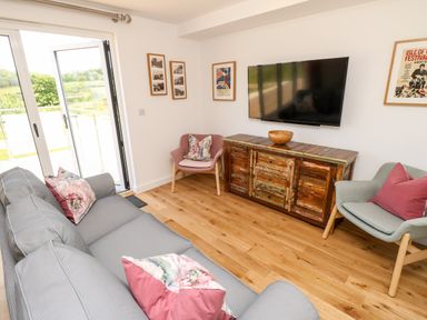 A living room with a gray sofa and two armchairs with cushions a wooden cabinet under a wall-mounted TV and framed pictures on the walls at Claret in Seaview