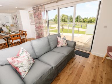 A living room with a gray sofa and floral cushions next to sliding glass doors opening onto a garden at Claret in Seaview