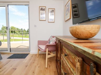 A room with a sliding glass door leading outside a pink chair with cushions two framed pictures on the wall a wooden cabinet with drawers a wooden bowl on the cabinet and a wall-mounted television at Claret in Seaview