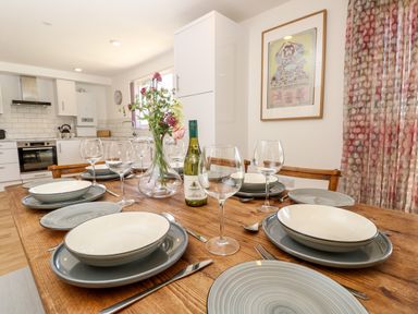 A dining table set with plates glasses cutlery a vase with flowers and a bottle of wine in a kitchen at Claret in Seaview