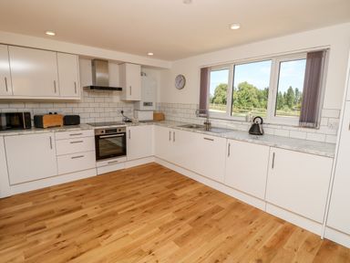 A kitchen with white cabinets wooden floor and a window showing trees at Claret in Seaview