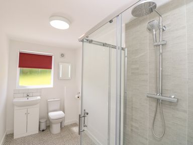 A bathroom with a shower, toilet, sink, mirror, red window blind and patterned floor tiles at Claret in Seaview