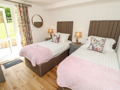 A bedroom with two single beds lamps a round mirror and floral curtains at Claret in Seaview