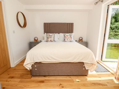A bedroom with a brown bed frame and headboard two floral pillows on the bed and two bedside tables with lamps at Claret in Seaview
