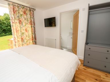 A bedroom with a bed covered in white bedding a floral curtain a wall mounted TV a grey dresser and an open door leading to a bathroom at Claret in Seaview
