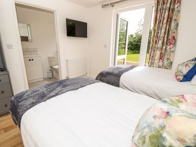 A bedroom with two single beds a wall-mounted TV an open door to a bathroom and a glass door opening to a garden at Claret in Seaview