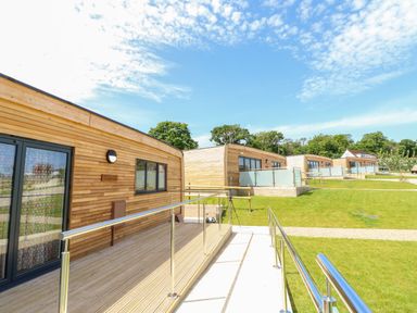 Wooden lodges with decks and metal railings on grass under a blue sky at Claret in Seaview