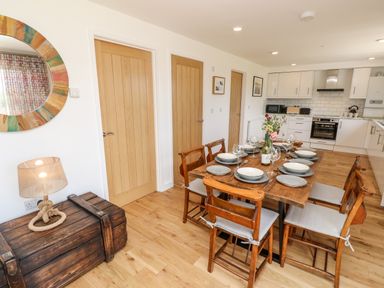 A dining area with a wooden table set with plates and glasses next to a kitchen with white cabinets and three wooden doors at Muscat in Seaview