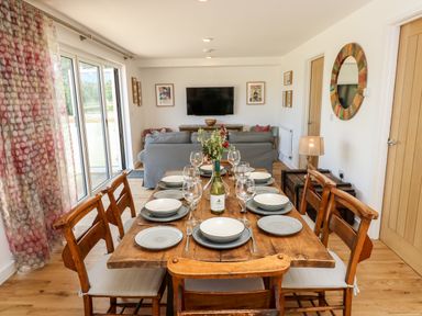 A dining table with plates glasses and a bottle in a living room with sofas and a wall mounted TV at Muscat Seaview