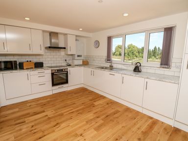 A kitchen with white cabinets wooden floor a window and various appliances at Muscat Seaview
