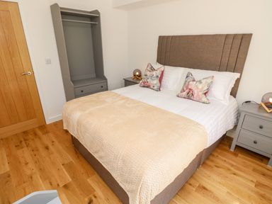 A bedroom with a double bed, two bedside tables with lamps, a wardrobe, and wooden flooring at Muscat Seaview