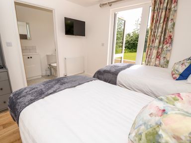 A bedroom with two single beds a wall-mounted TV an open door to a bathroom and a door leading outside with floral curtains at Muscat Seaview