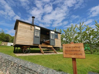 A small wooden cabin on wheels with open doors and steps leading to the entrance in a grassy area with a sign about private parking at Merlot Pondwell near Seaview