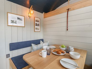 A dining nook with wooden table blue bench seating porcelain dishes and framed pictures on the wall at Merlot Pondwell near Seaview