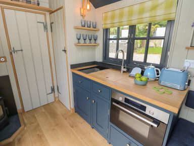 A kitchen with blue cabinets wooden countertop oven sink window with yellow plaid blind and blue appliances at Merlot in Pondwell near Seaview