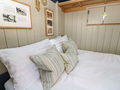 A bed with white pillows and patterned cushions in a room with wooden paneled walls and framed pictures at Merlot Pondwell near Seaview