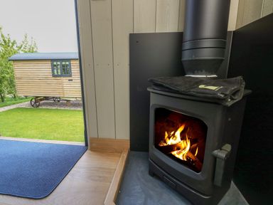 A wood burning stove with fire inside next to an open door showing a small wooden cabin outside at Merlot in Pondwell near Seaview