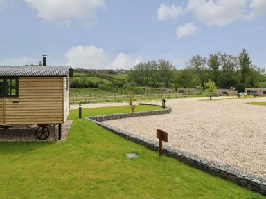 A small wooden cabin on wheels next to gravel paths and green grass with trees and houses in the background at Merlot Pondwell near Seaview
