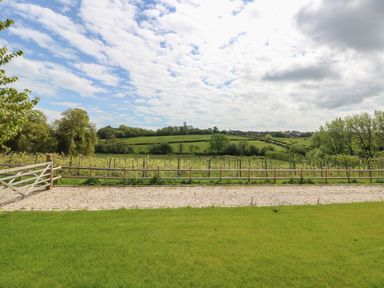 A grassy yard with a gravel path and wooden fence overlooking green fields and trees at Merlot in Pondwell near Seaview