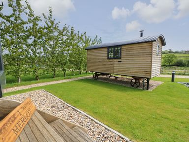 A wooden shepherd hut on wheels on grass near a pathway with trees in the background at Merlot in Pondwell near Seaview