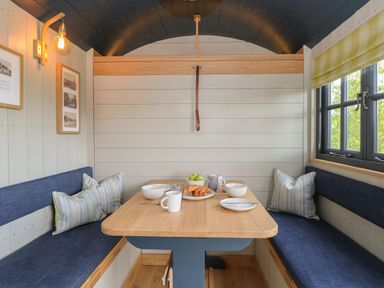 A dining nook with a wooden table and bench seating with cushions bowls cups plates and croissants on table at Malbec Pondwell near Seaview