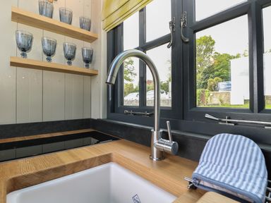 A kitchen sink with a modern faucet next to a window and shelves with blue glasses at Malbec Pondwell near Seaview