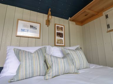 A bed with striped pillows against a wooden paneled wall with framed pictures and a light fixture at Malbec in Pondwell near Seaview
