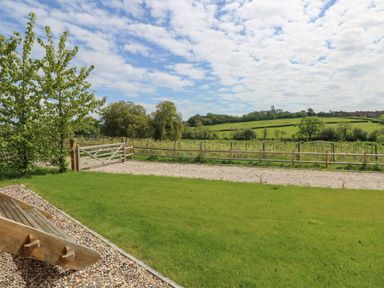 A garden with green lawn wooden gate and fenced field under a partly cloudy sky at Malbec Pondwell near Seaview