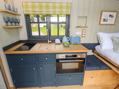 A kitchenette with blue cabinets wooden countertop and a window above the sink at Malbec Pondwell near Seaview