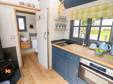 A kitchen with blue cabinets wooden countertop a sink stove oven window and a door leading to a bathroom at Malbec Pondwell near Seaview