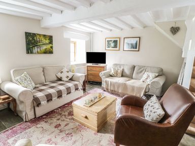 A living room with two beige sofas a brown leather armchair a wooden chest coffee table and a small wooden cabinet with a television at Tan Y Garth Cottage in Glyndyfrdwy near Llangollen