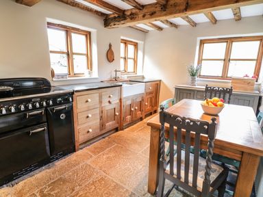 A kitchen with wooden cabinets a black stove a wooden dining table with chairs and a fruit bowl at Tan Y Garth Cottage in Glyndyfrdwy near Llangollen