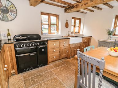 A kitchen with wooden cabinets a black oven a farmhouse sink stone tile flooring and a wooden dining table with chairs at Tan Y Garth Cottage in Glyndyfrdwy near Llangollen