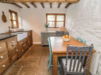 A kitchen with wooden cabinets a wooden table with chairs and a bowl of fruit at Tan Y Garth Cottage in Glyndyfrdwy near Llangollen
