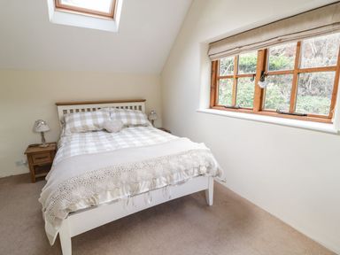 A bedroom with a bed and checked bedding next to a window at Tan Y Garth Cottage in Glyndyfrdwy near Llangollen