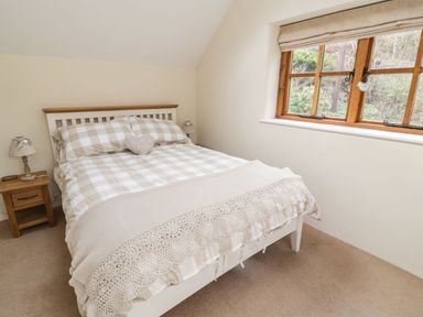 A bedroom with a bed with checkered bedding beside a wooden nightstand and a window at Tan Y Garth Cottage in Glyndyfrdwy near Llangollen