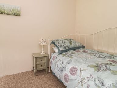 A bedroom with a single bed with floral bedding a bedside table with a lamp and a painting on the wall at Tan Y Garth Cottage in Glyndyfrdwy near Llangollen