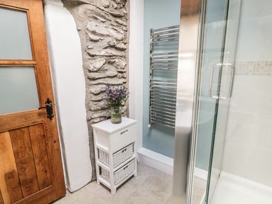 A bathroom corner with a wooden door stone wall white cabinet with flowers and a metal towel rack at Tan Y Garth Cottage in Glyndyfrdwy near Llangollen