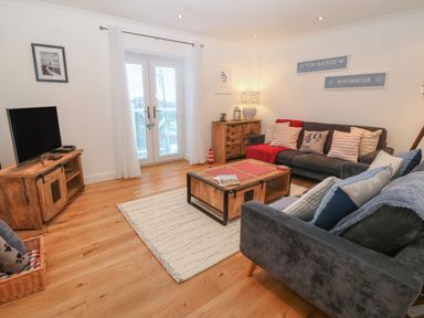 A living room with two sofas a wooden coffee table a media console with a television and glass doors at 8 Pen Llanw Tides Reach in Rhosneigr