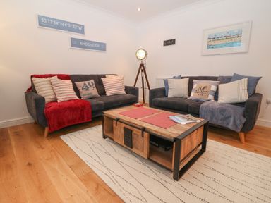 A living room with two sofas a wooden coffee table a floor lamp and wall art at 8 Pen Llanw Tides Reach in Rhosneigr