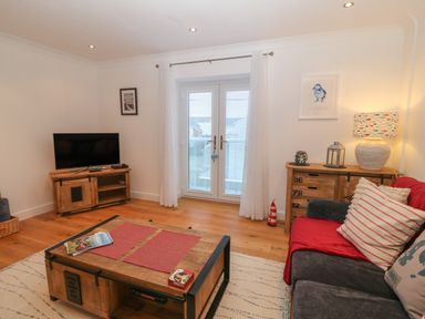 A living room with a sofa a wooden coffee table a TV on a wooden stand and a wooden cabinet with a lamp at 8 Pen Llanw Tides Reach in Rhosneigr